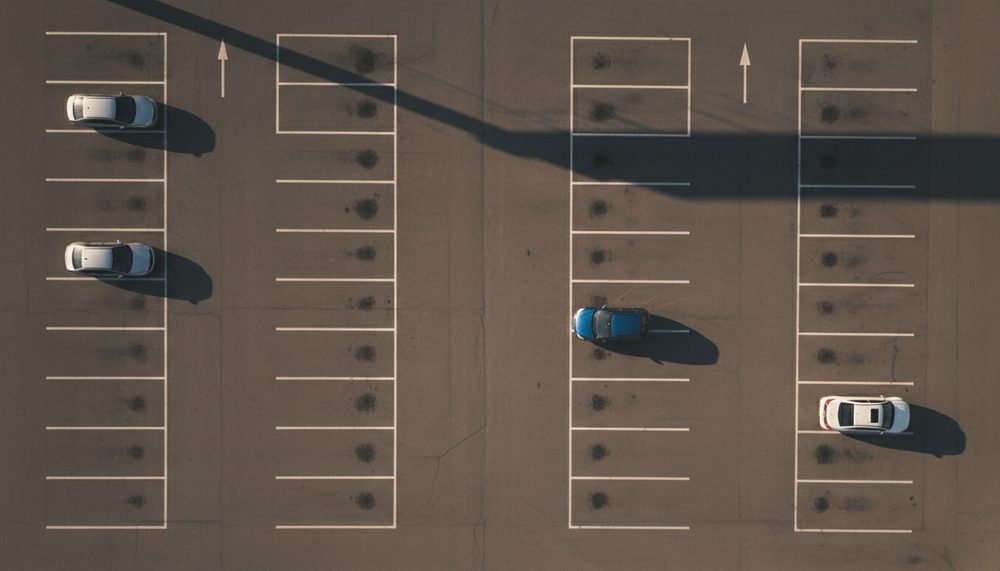 A mostly empty parking lot with crisp painted bays, three cars in separated spaces, seen from above.